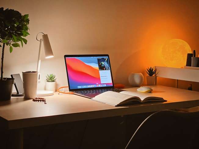 Un bureau éclairé par des lampes de chevet avec un livre ouvert et un ordinateur portable