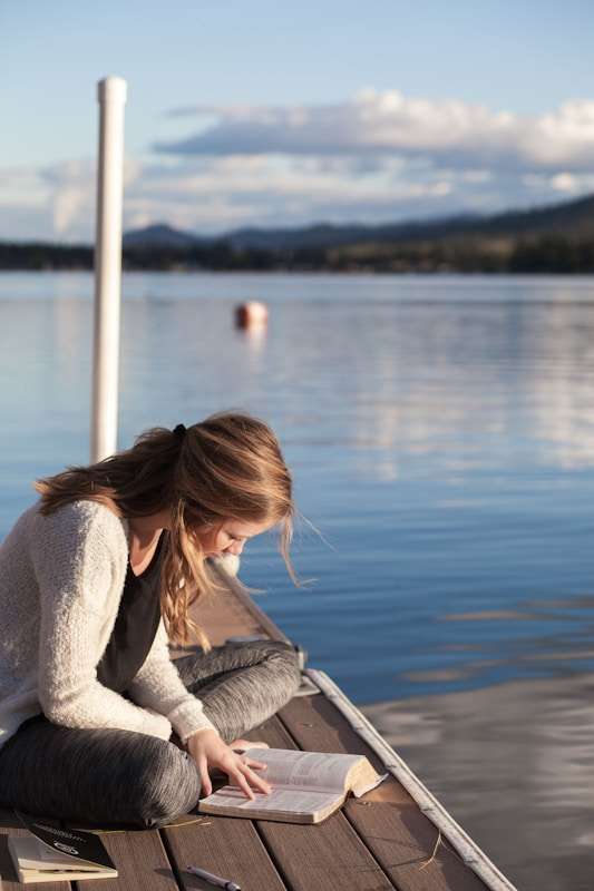 Une femme lisant un livre sur un ponton au bord de l'eau